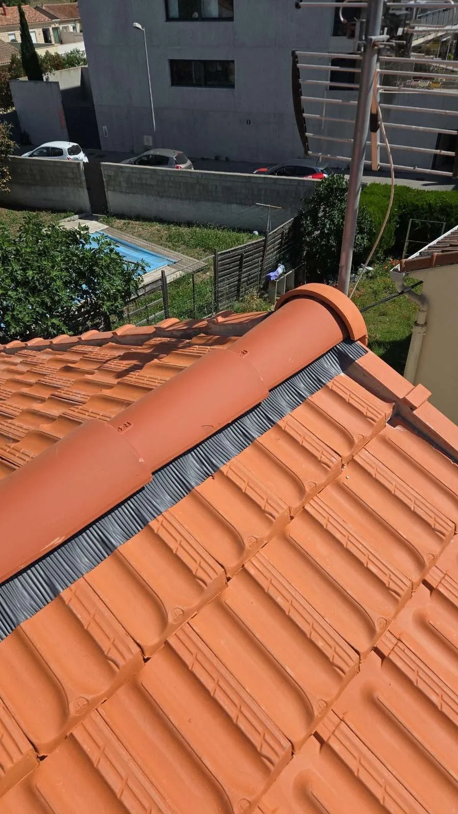 Tuiles faîtières en terre cuite et closoir visibles au sommet d’une toiture