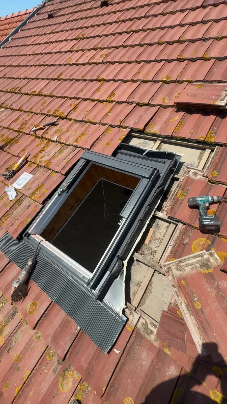 Fenêtre de toit ouverte en cours d’installation, entourée de tuiles et d’outils