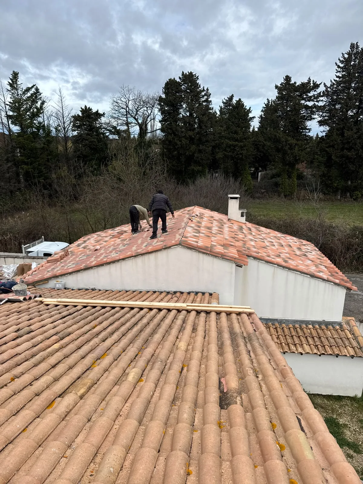 Deux personnes sur un pan de toiture en tuiles, avec une autre couverture au premier plan